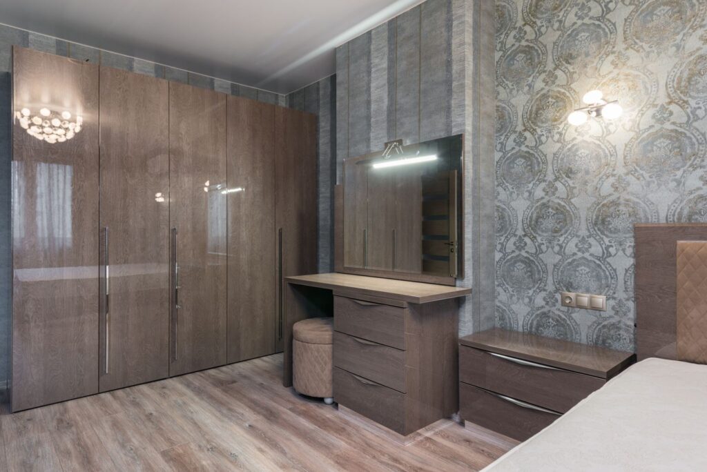 Glossy cupboard with chest of drawers and mirror near a bed